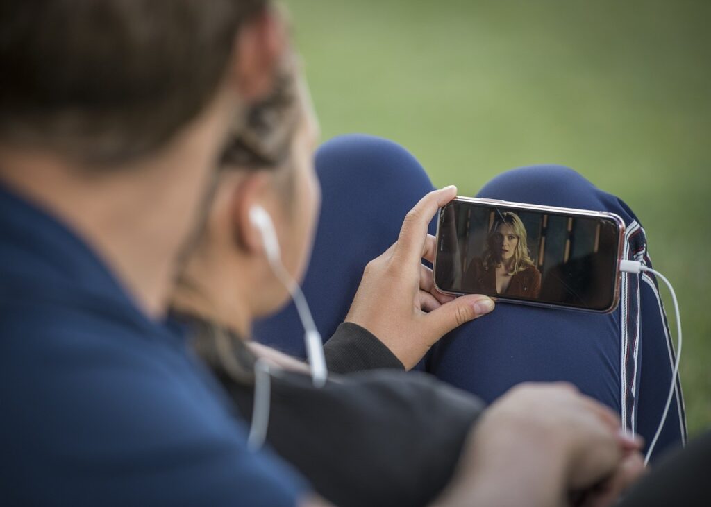 hero attention video mobile Personne regardant une vidéo sur son smartphone avec des écouteurs, assise en extérieur