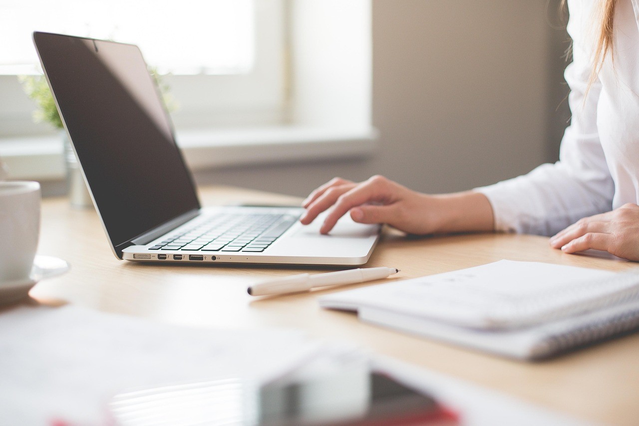 Person taking notes in a notebook next to a laptop, keeping a decision log