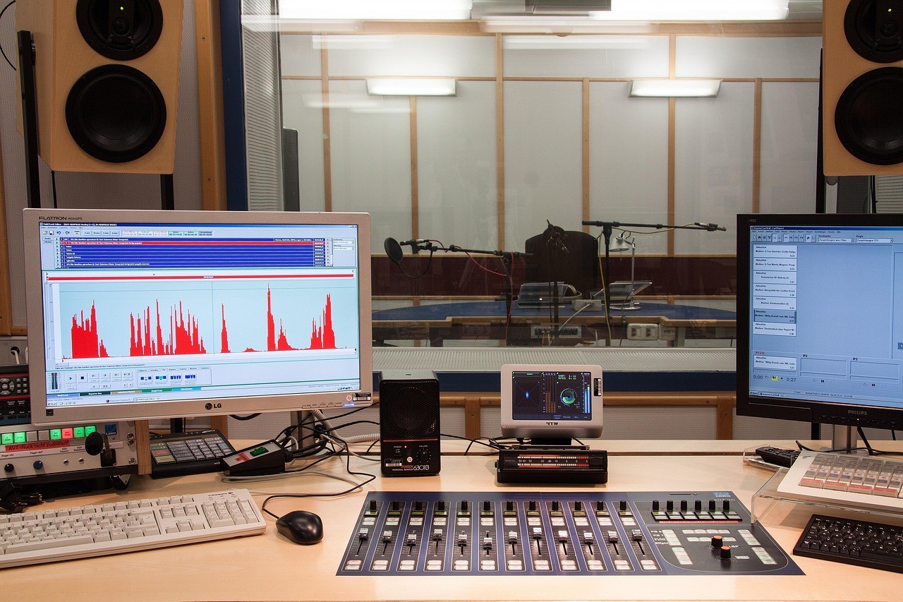 A video and audio production desk with multiple monitors showing waveform edits
